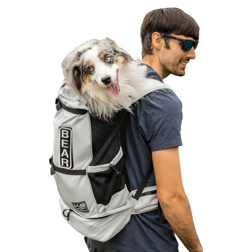 Man hiking with an Australian Shepherd riding forward-facing in the white K9 Sport Sack Knavigate dog carrier backpack