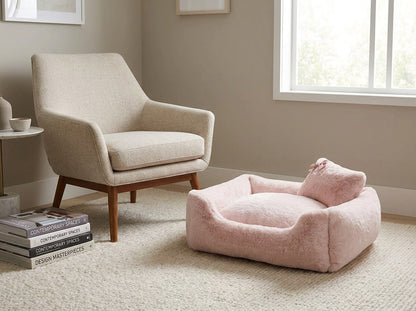 Divine bolster dog bed in Blush styled in a living room corner beside an armchair